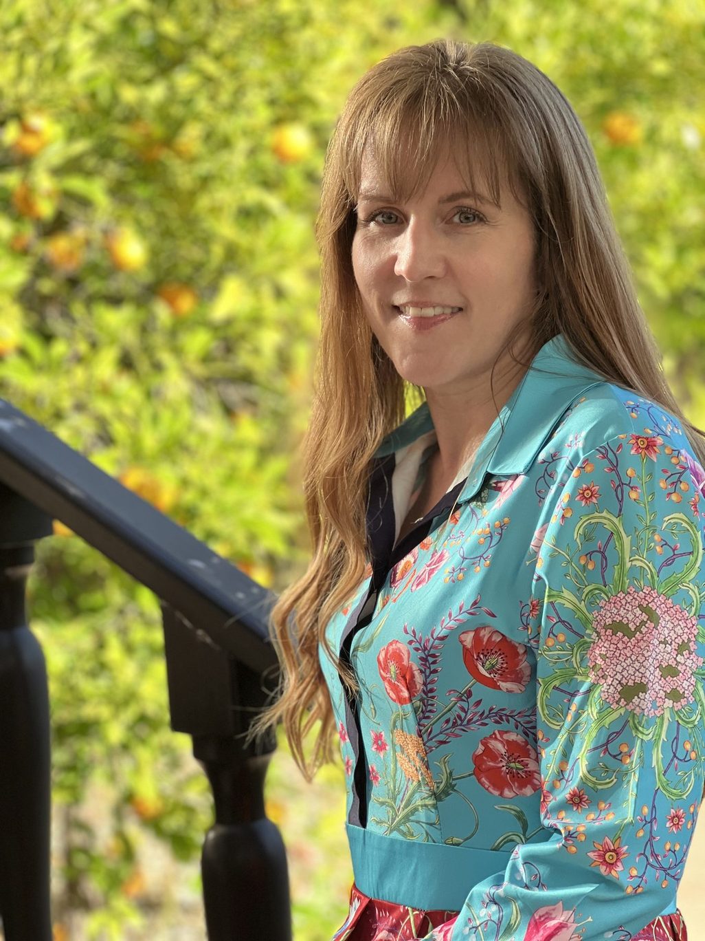Heather Logghe, MD, smiling beside a stair rail in front of an orange tree