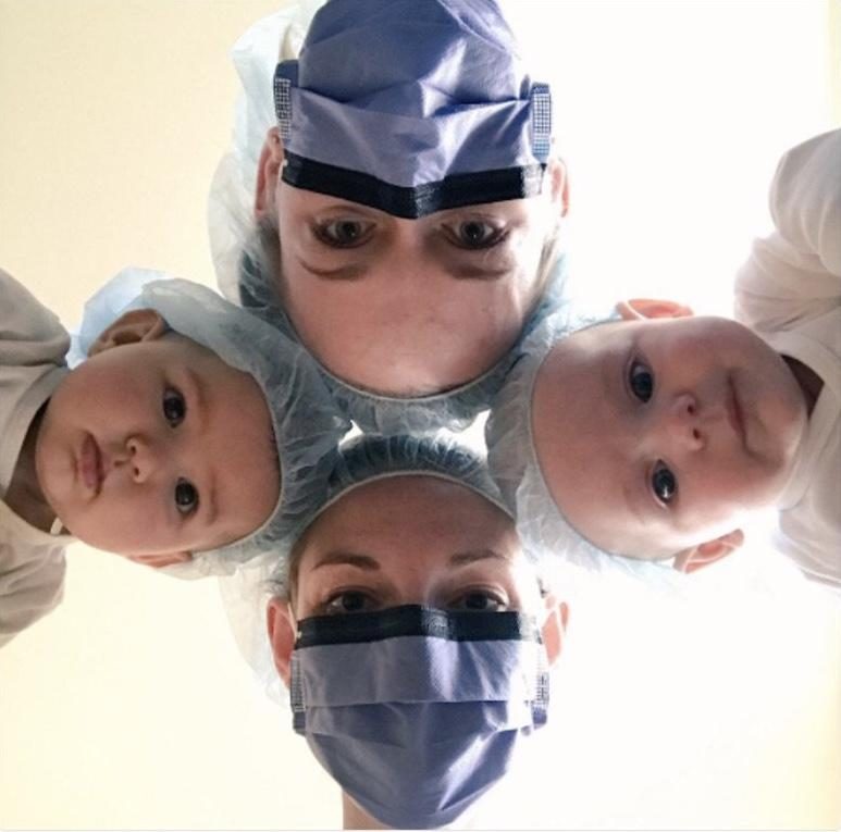 A surgeon and two babies in surgical caps looking down at the camera