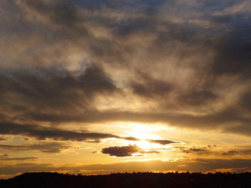 Late sun breaking through heavy clouds over a dark ridge