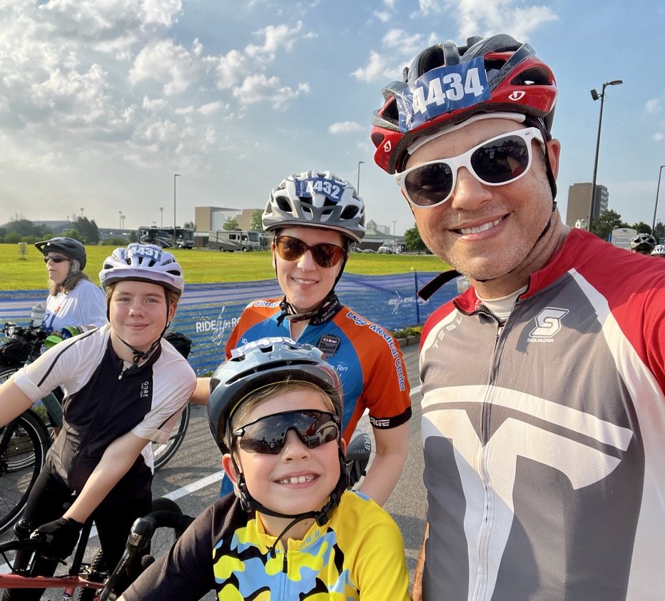 Heather, her husband, and their two kids in bike helmets, smiling at the start of the Ride for Roswell