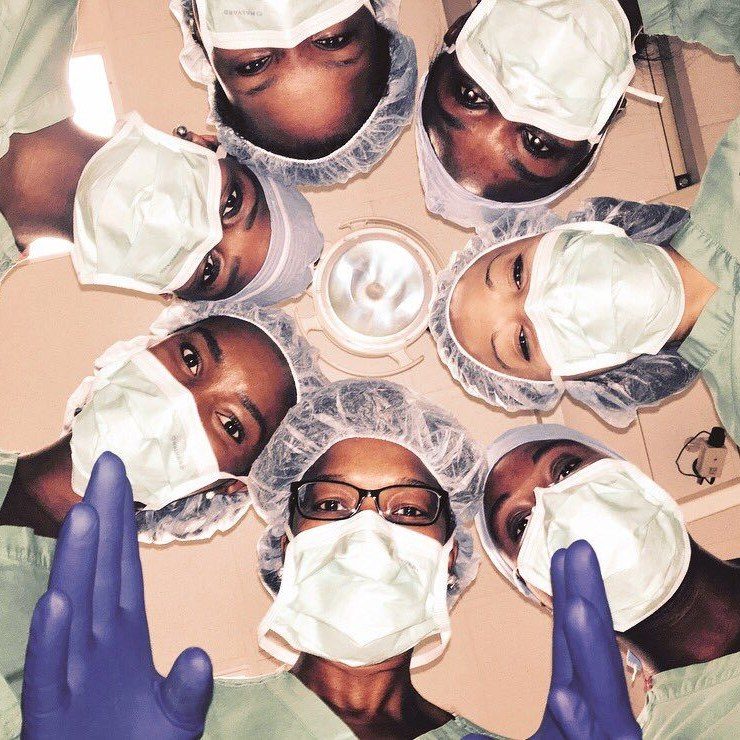 Surgeons in masks and caps in a circle looking down at the camera, recreating the New Yorker cover for #NYerORCoverChallenge